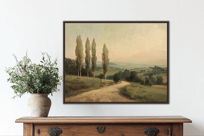 Framed landscape painting on a wall above a wooden dresser with a plant.