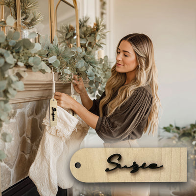 Woman decorating a fireplace with greenery and a wooden name tag in a cozy indoor setting.