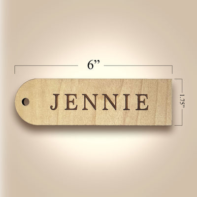 Wooden name tag with 'JENNIE' engraved, shown with dimensions on a beige background