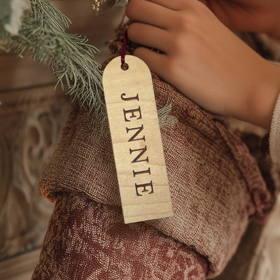 "Engraved wooden stocking tag with custom vertical name, hanging on a red knit Christmas stocking."