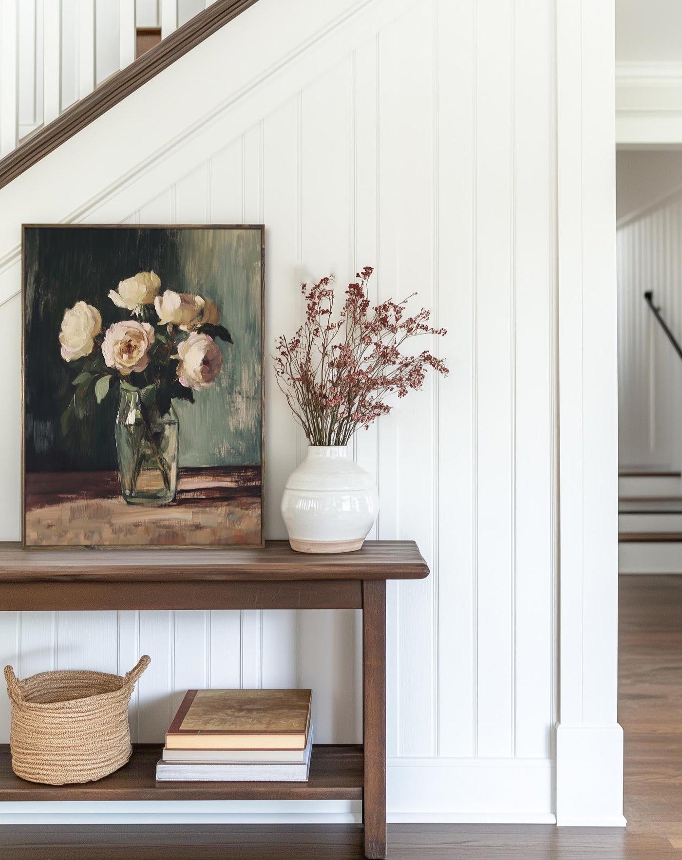Nook with a wooden shelf holding a vase of flowers, books, and a basket, with a painting in the background.