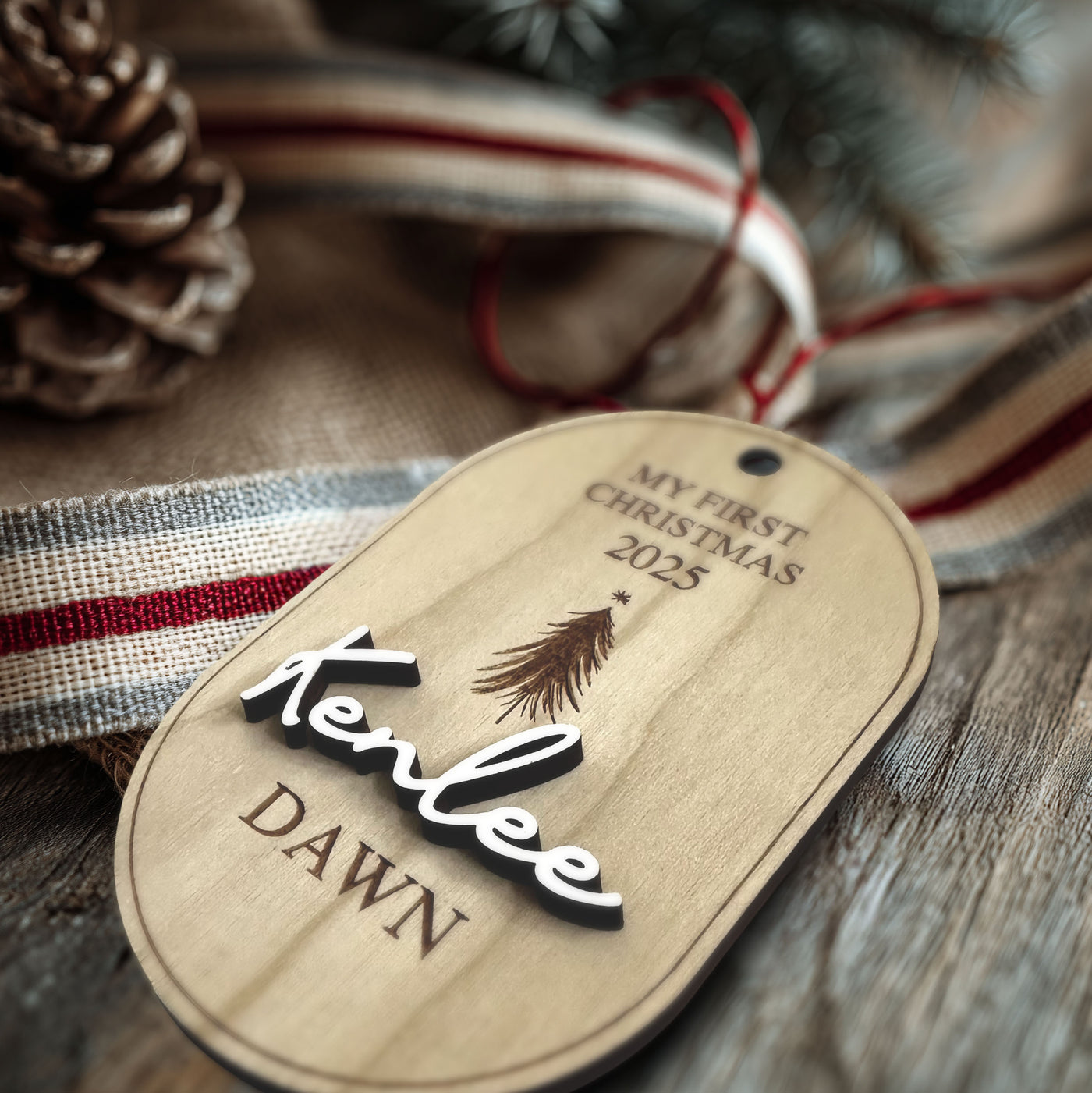 Wooden tag with 'My First Christmas 2025' and 'Kenlee Dawn' text, surrounded by festive elements.