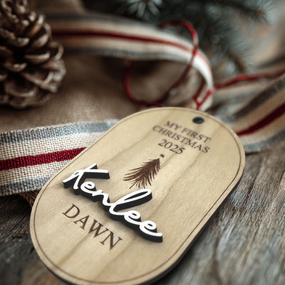 Wooden tag with 'My First Christmas 2025' and 'Kenlee Dawn' text, surrounded by festive elements.