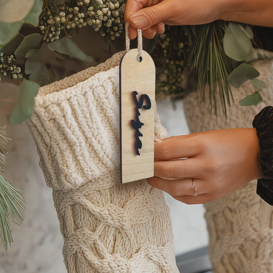 "Modern personalized wood stocking tag with custom cut-out vertical name, hanging on a knitted Christmas stocking."