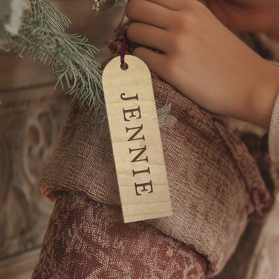 "Engraved wooden stocking tag with custom vertical name, hanging on a red knit Christmas stocking."